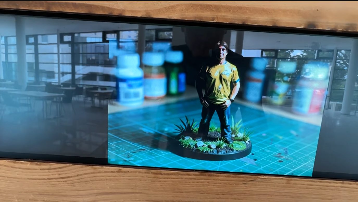 Still frame: a guest as a painted tabletop miniature on a base, shown on the photo booth screen